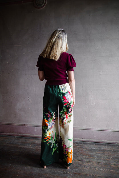 Image featuring a woman wearing the linen blend Aggie pants by Alemais with an elastic waist, wide leg and an allover tropical floral print.