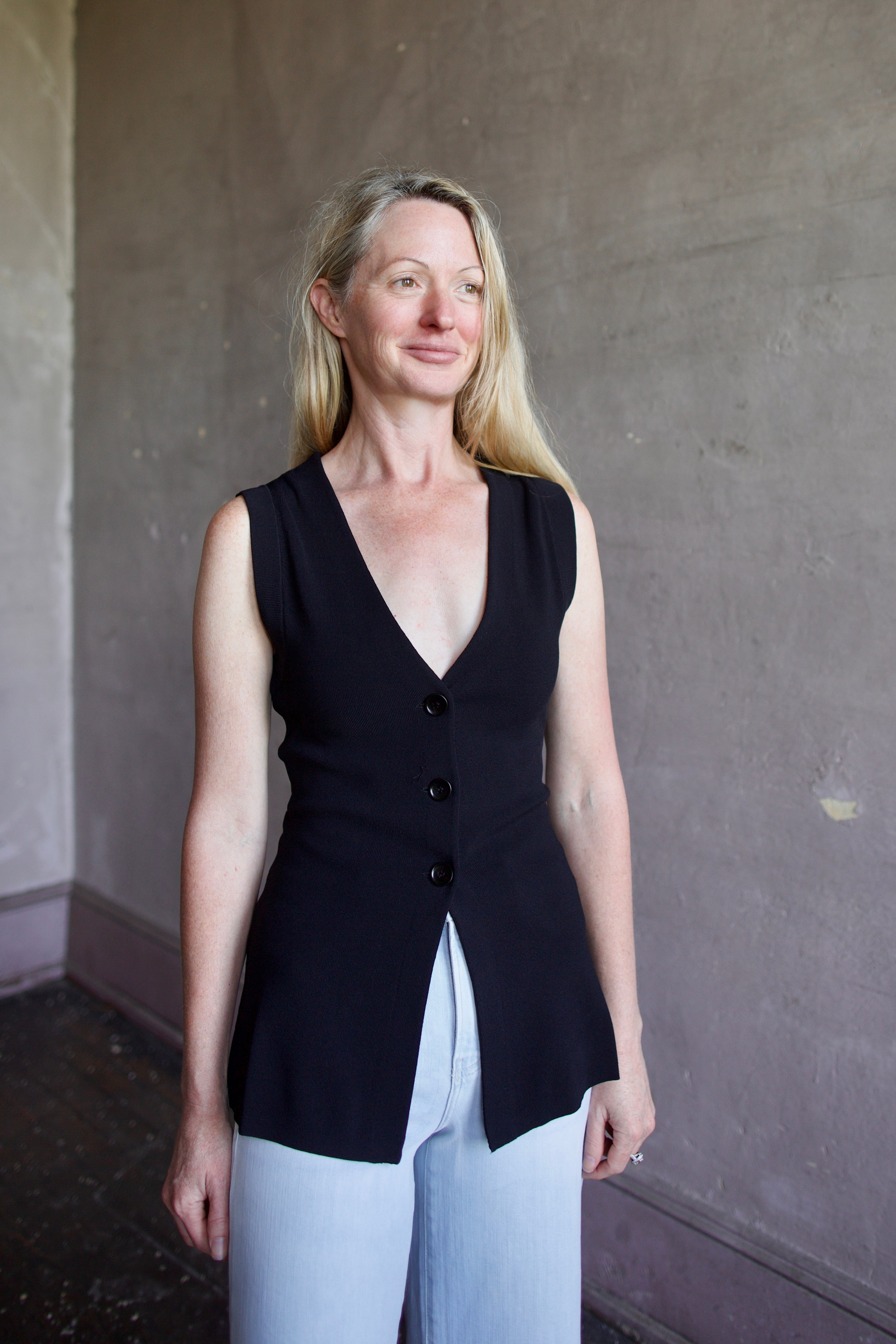 Mature woman wearing a flattering Apiece Apart Marca Knit Top in black with 3 button closure, v- neck and sleeveless