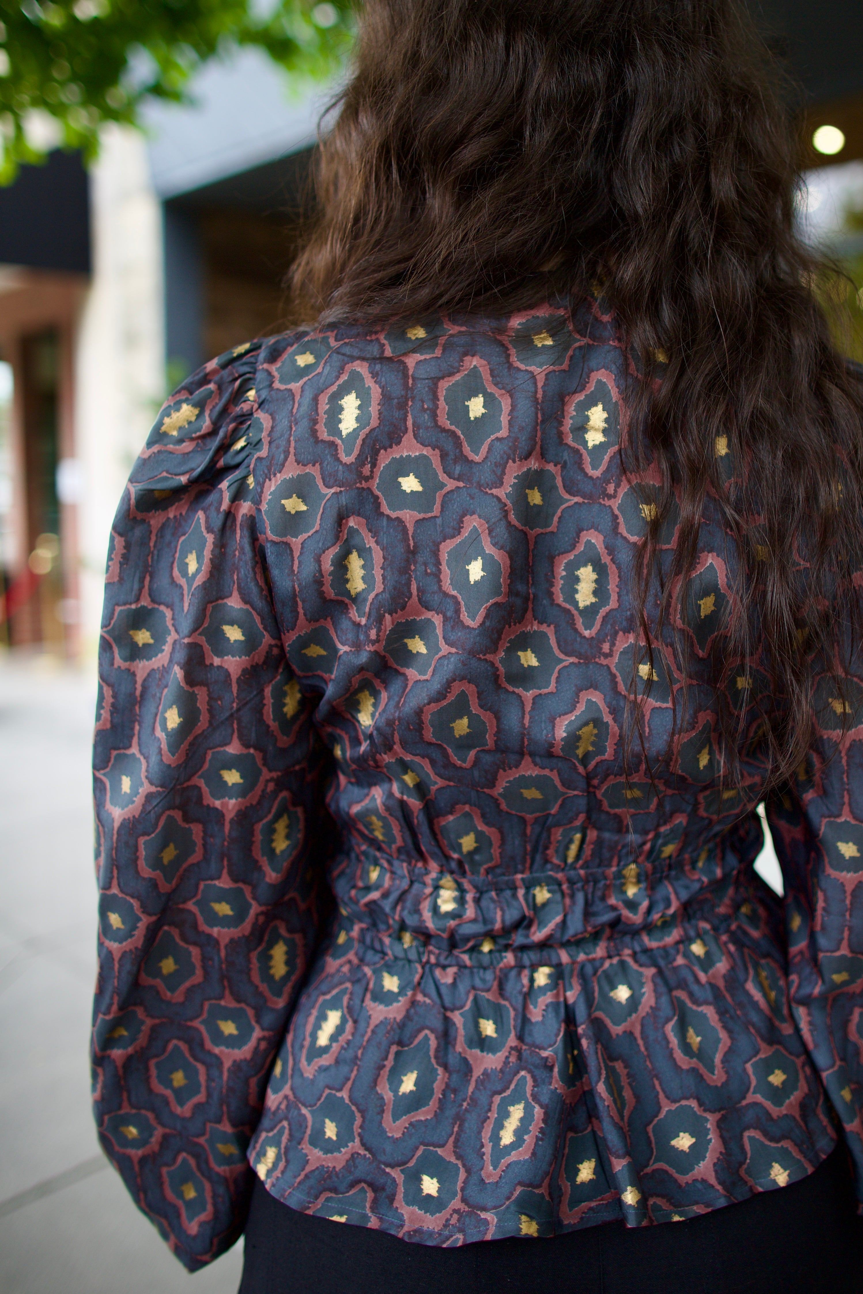 Image of a woman wearing the Hannah Artwear silk Lola Blouse with peplum, long sleeves, v-neck, blockprint and hand applied gold leaf