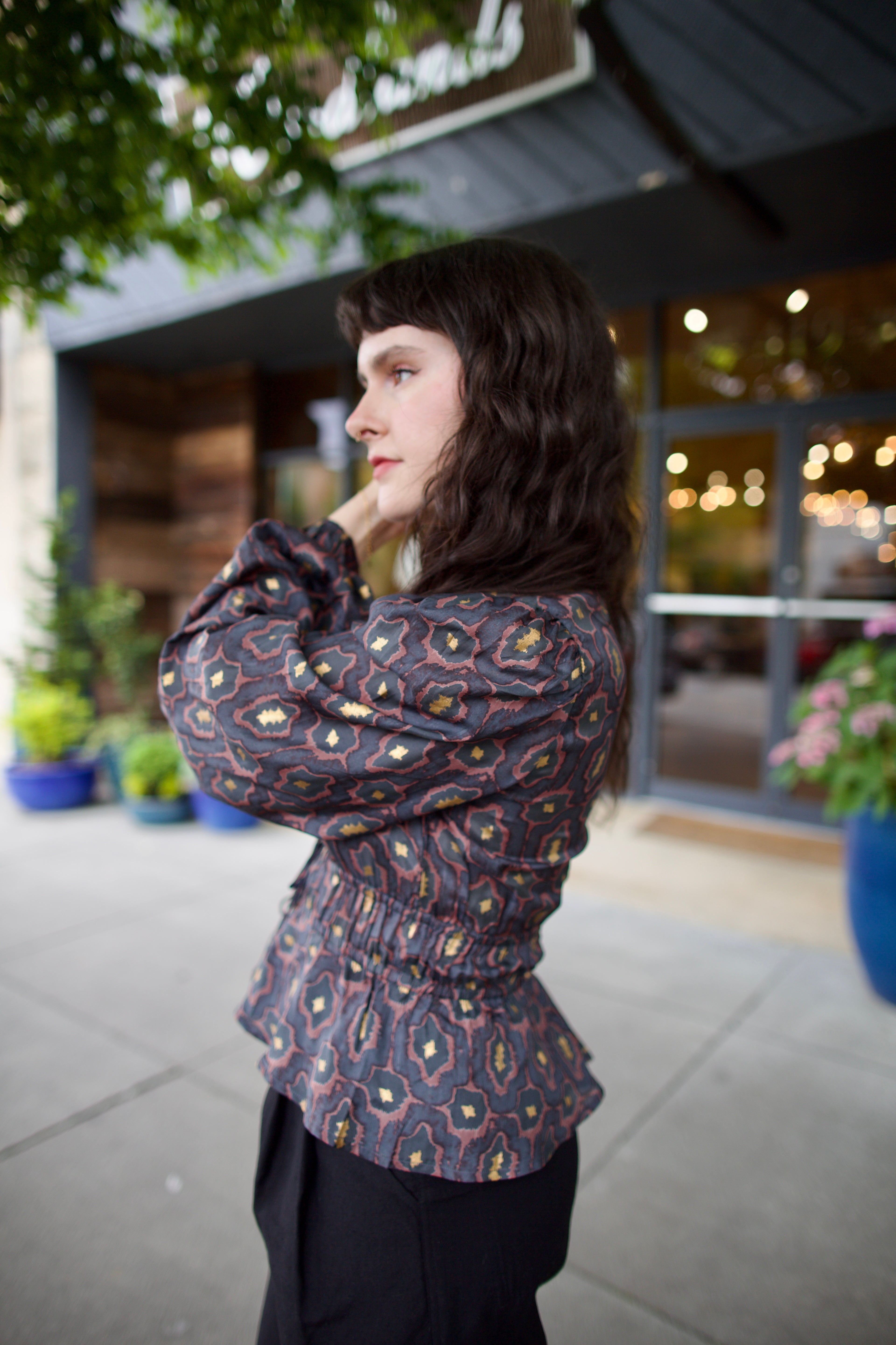 Image of a woman wearing the Hannah Artwear silk Lola Blouse with peplum, long sleeves, v-neck, blockprint and hand applied gold leaf