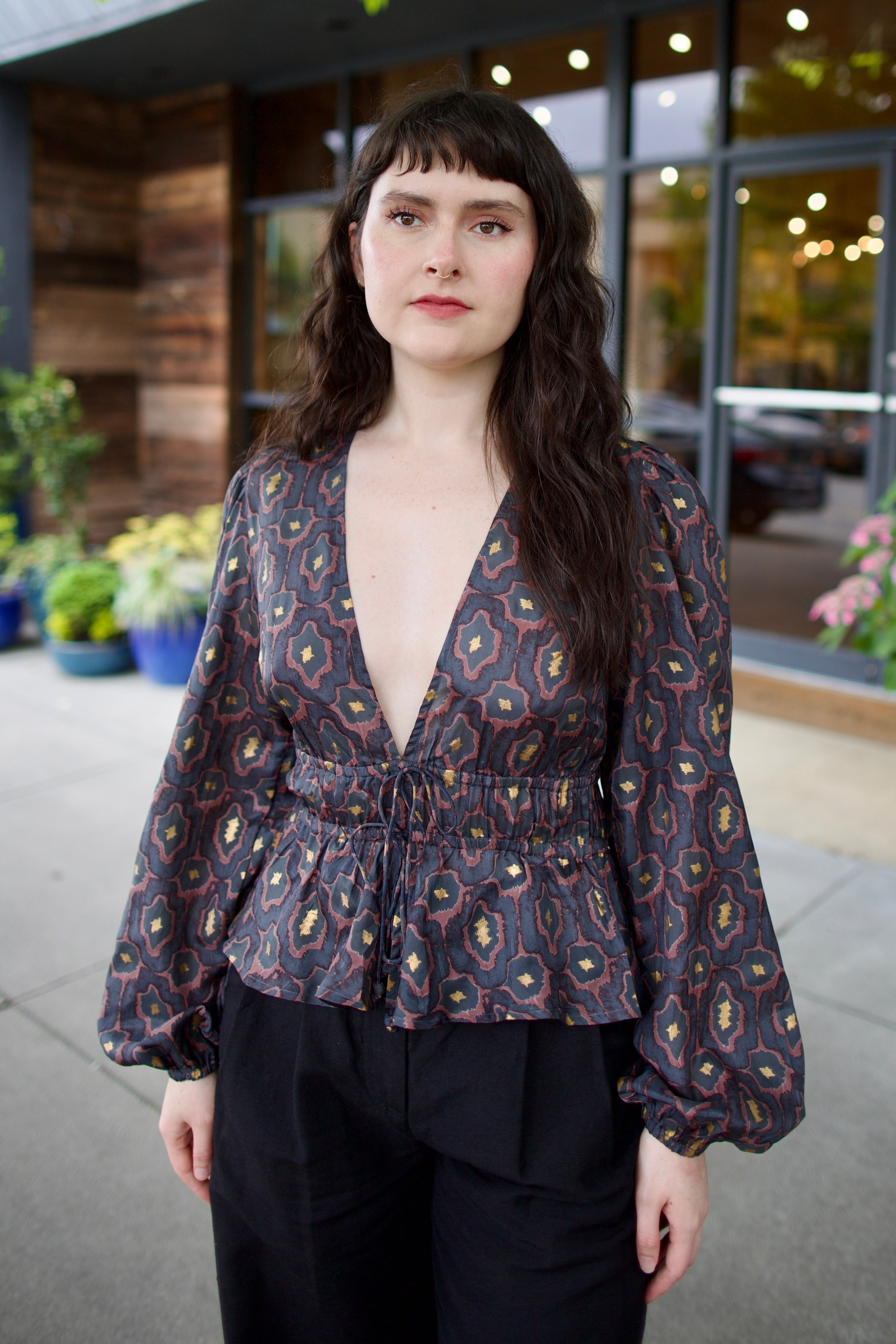Image of a woman wearing the Hannah Artwear silk Lola Blouse with peplum, long sleeves, v-neck, blockprint and hand applied gold leaf