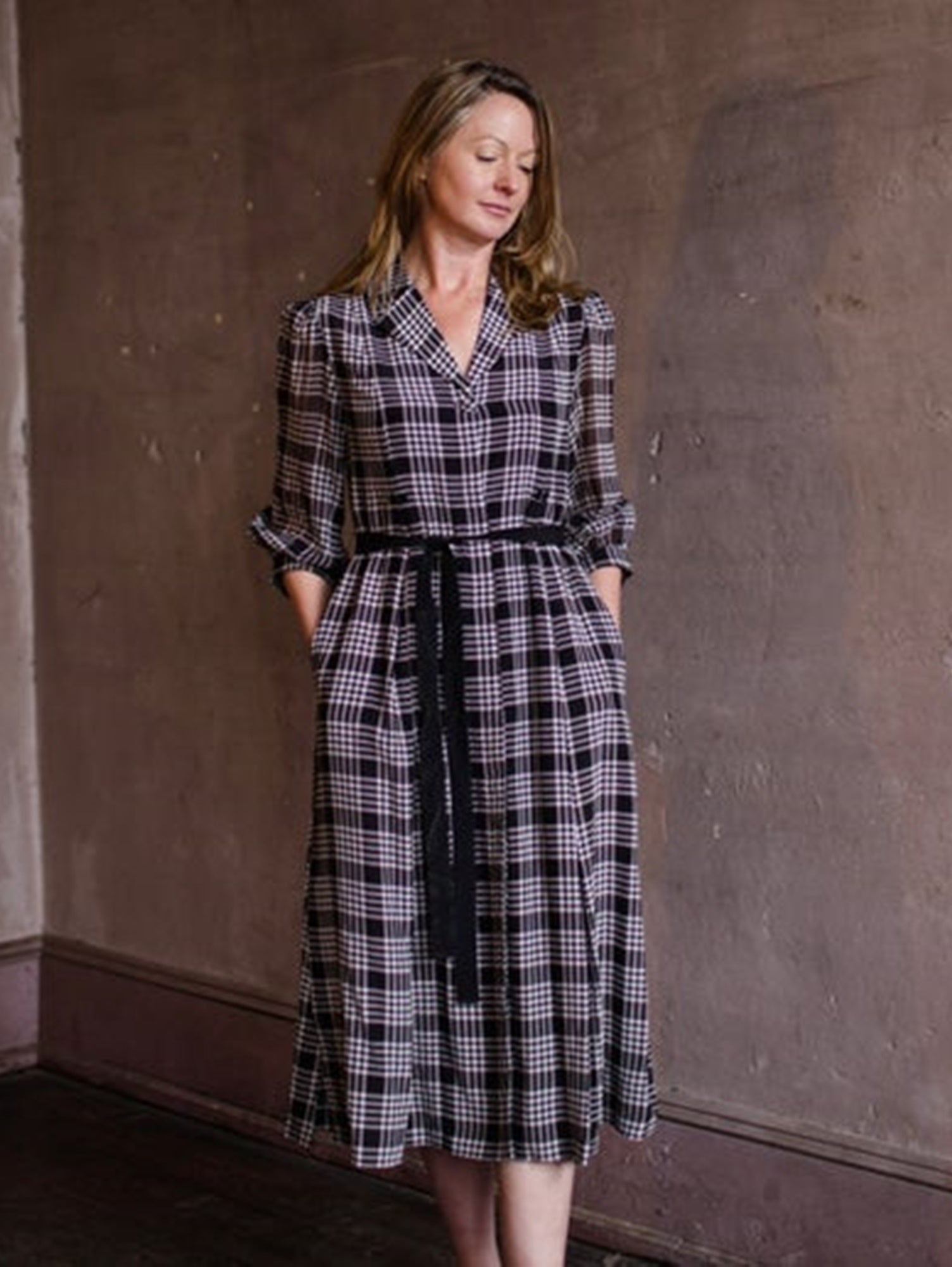 Image featuring a woman wearing a silk black and white plaid dress by Jessie Liu with a classic A-line, tie waist and midi hem.