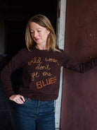 Image featuring a woman wearing the brown cashmere sweater by Lingua Franca with a crew neckline, long sleeves, and "Wild women don't get the blues" embroidered on front.