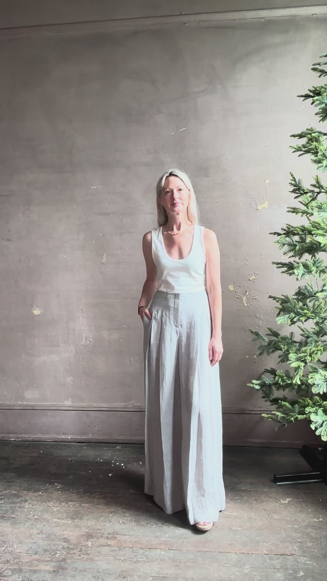 Mature woman reviewing effortless women's designer Drew wide leg Trouser from TWP rendered in a versatile light heather grey and crafted from light weight hemp with high-rise, drop waist pleats, and side seam pockets, and made in the USA
