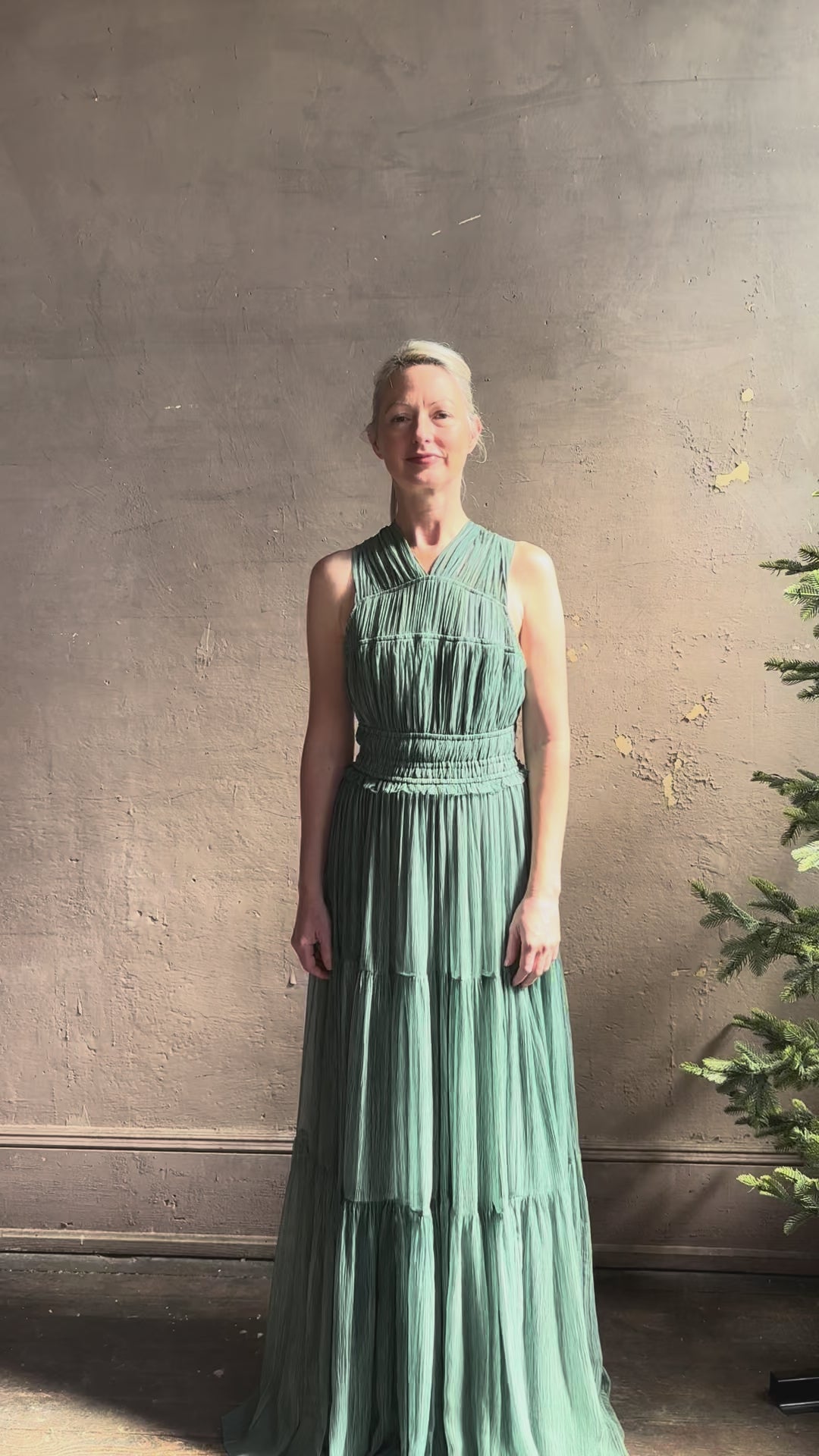 Woman reviewing Freesia Gown from Ulla Johnson rendered in a soft green and crafted from luxurious silk crinkle chiffon with low back and flexible waistband