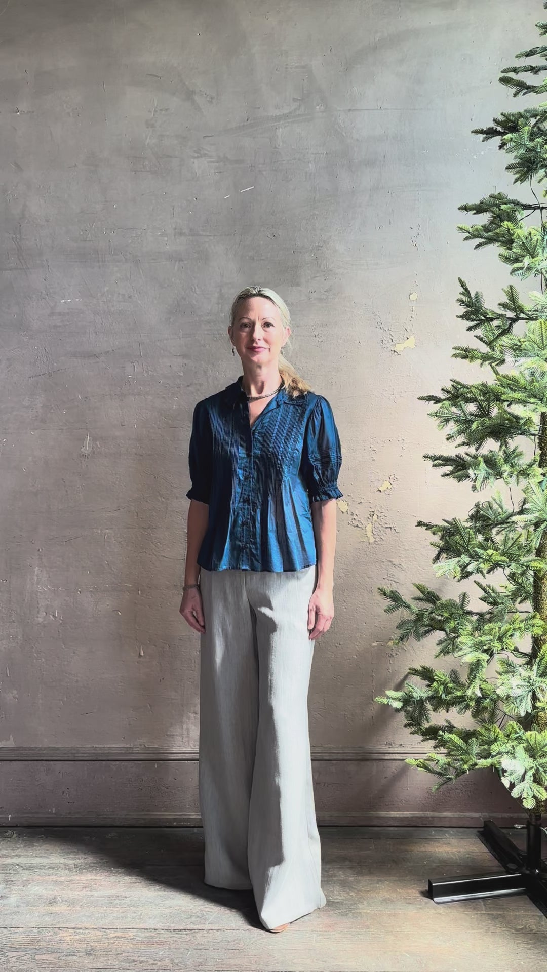 Mature woman reviewing Jess Blouse from Trovata rendered in a classic  Navy blue and crafted from light weight cotton poplin with short sleeves, peter pan collar, v-neck button front with intricate pintucking details at front and back