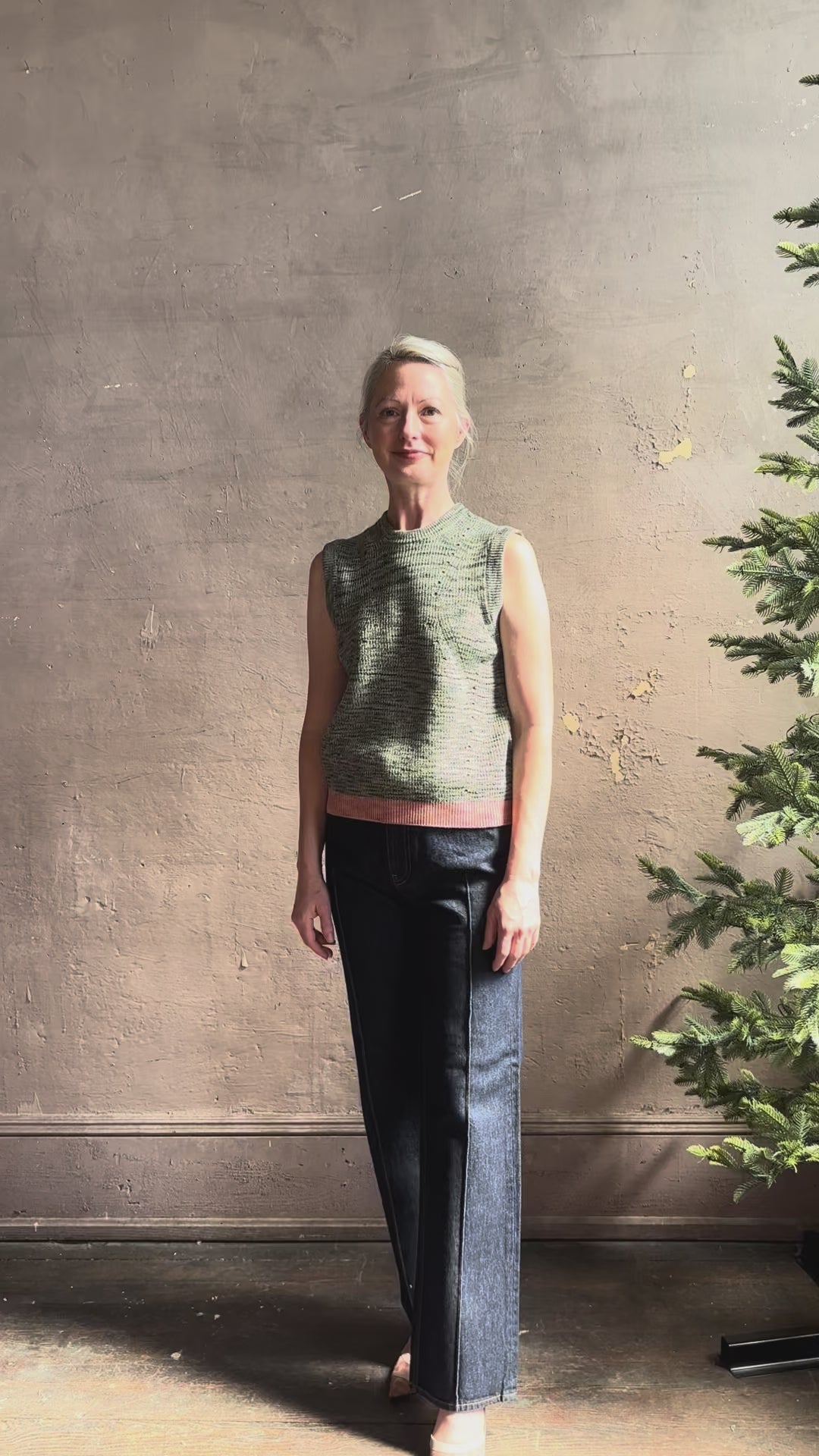 Mature model reviewing Margot sleeveless Knit Top from Ulla Johnson rendered in a two tone heathered green and crafted from 100% cotton wth a crew neck and contrasting coral band at bottom