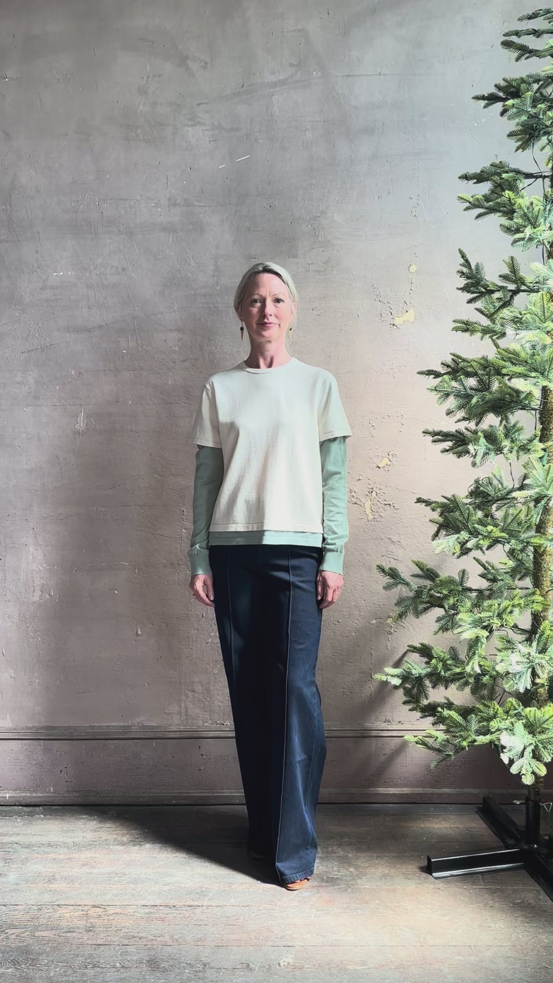 Mature woman reviewing elevated luxury Layer Tee Shirt from Guest in Residence rendered in a soft sage brush green and cream colorway and crafted from an exceptional blend of cotton, cashmere, and silk with long sleeves and a crew neckline