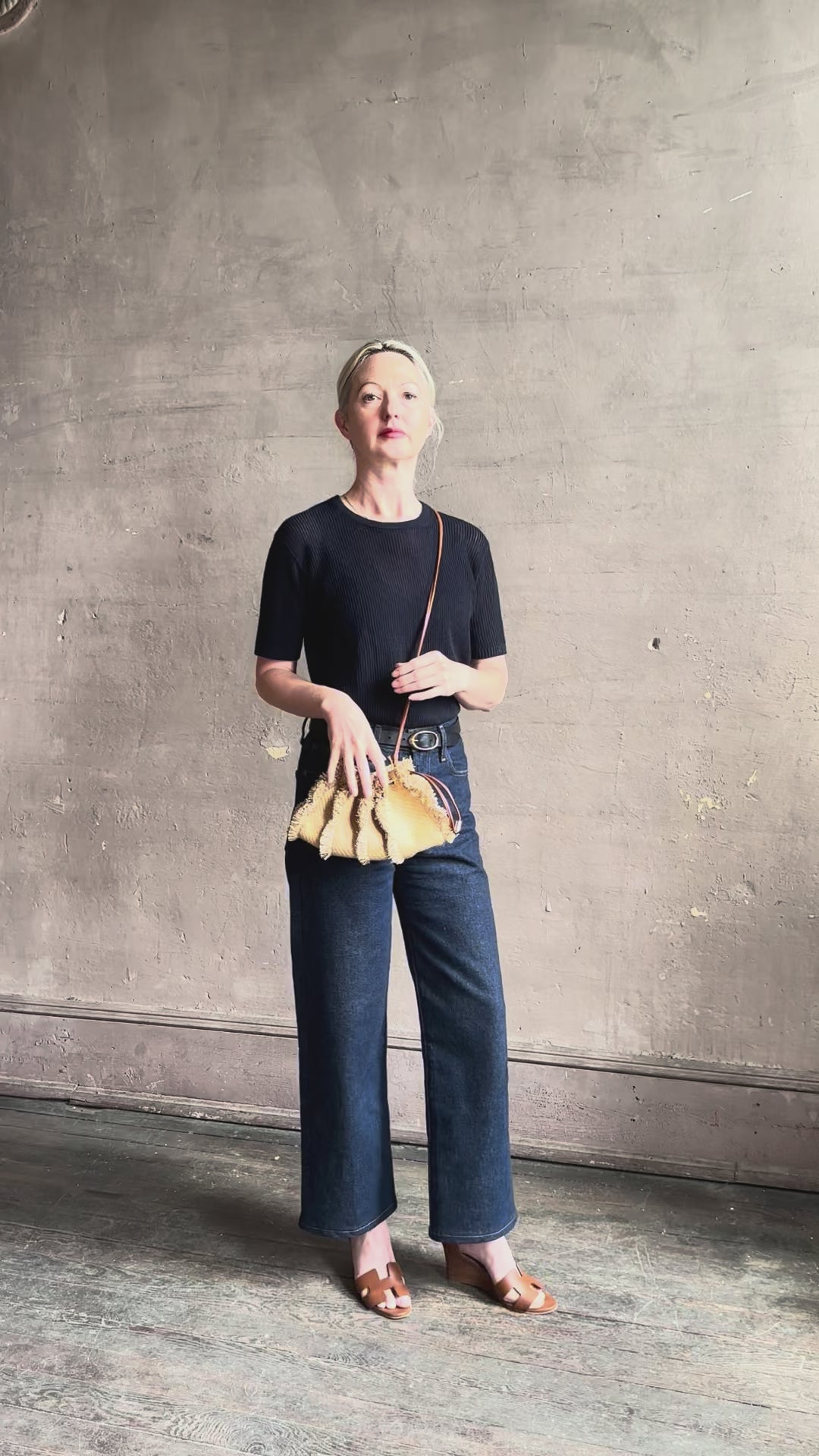 Mature woman reviewing designer Ulla Johnson Adria crossbody bag with raffia-textured exterior and removeable handle that can double as a clutch in a warm neutral tone