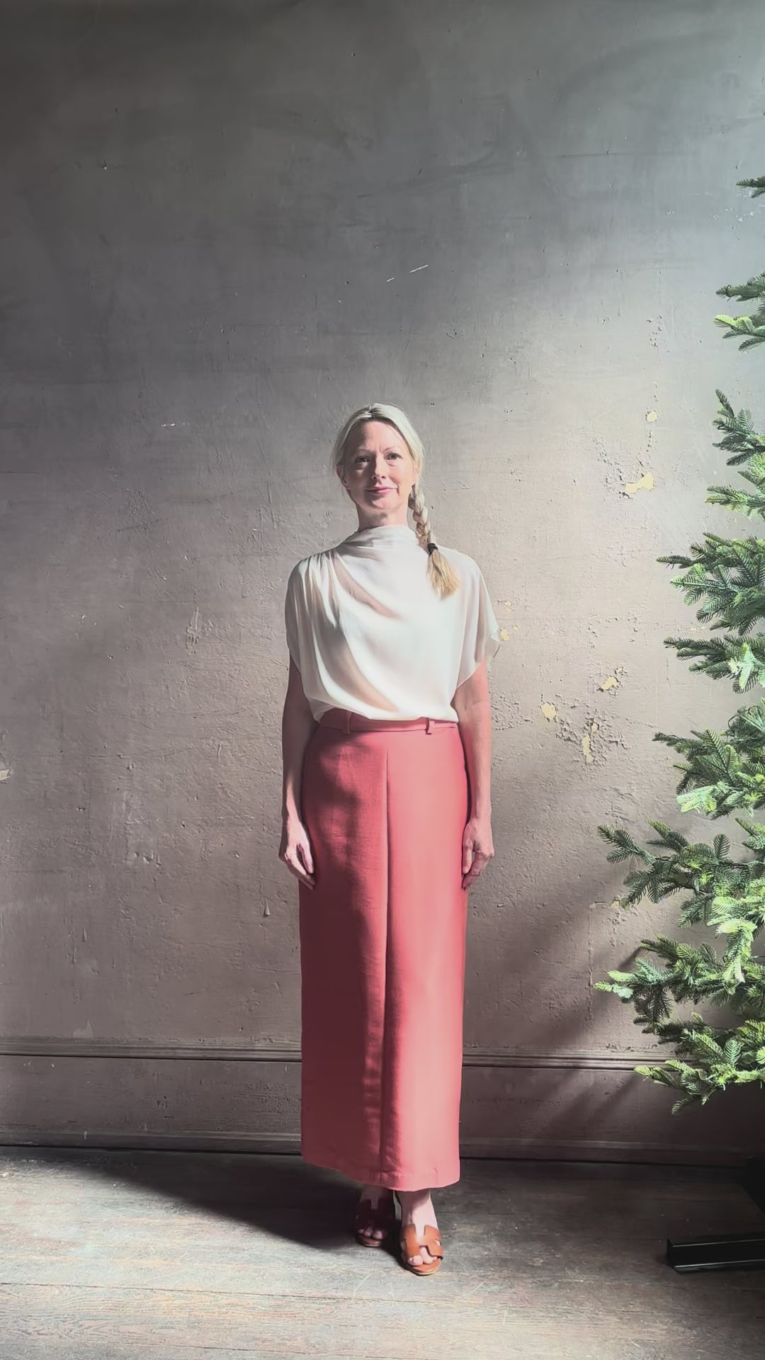 Mature woman reviewing an elevated soft blush TWP silk blouse with beautifully draped short sleeves and modern asymmetrical design