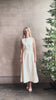 Mature woman reviewing elegant Crew Neck maxi A-Line Dress with Darts from TWP rendered in a soft off white and crafted in the USA from a viscose and linen fabric blend with side seam pockets and sleeveless