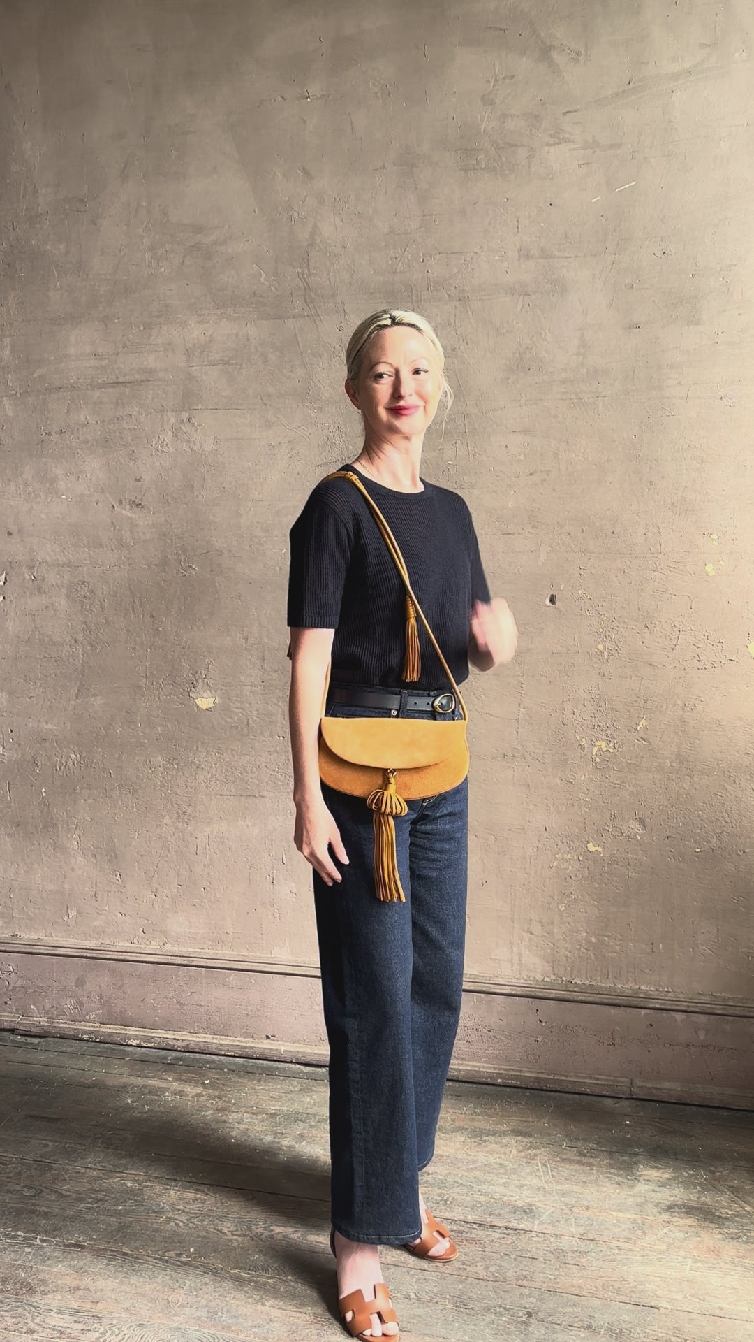 Mature woman reviewing the luxury Italian leather  Paloma handbag with Tassel Flap from Ulla Johnson rendered in a rich caramel brown featuring a pull tassel magnetic snap closure and removable adjustable handle that seamlessly converts to a designer clutch