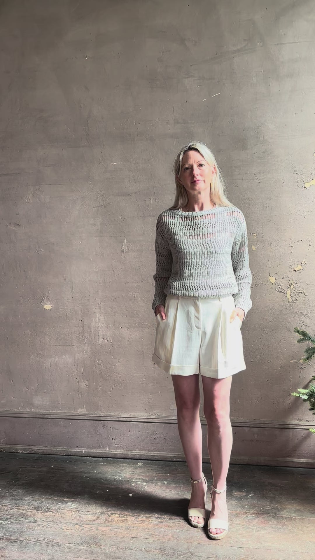 Mature woman reviewing elevated tailored Cisco Shorts from TWP rendered in a soft bone white and crafted in the USA using a viscose and  linen blend fabric with side seam pockets, belt loops, single front pleat and cuffed at the bottom