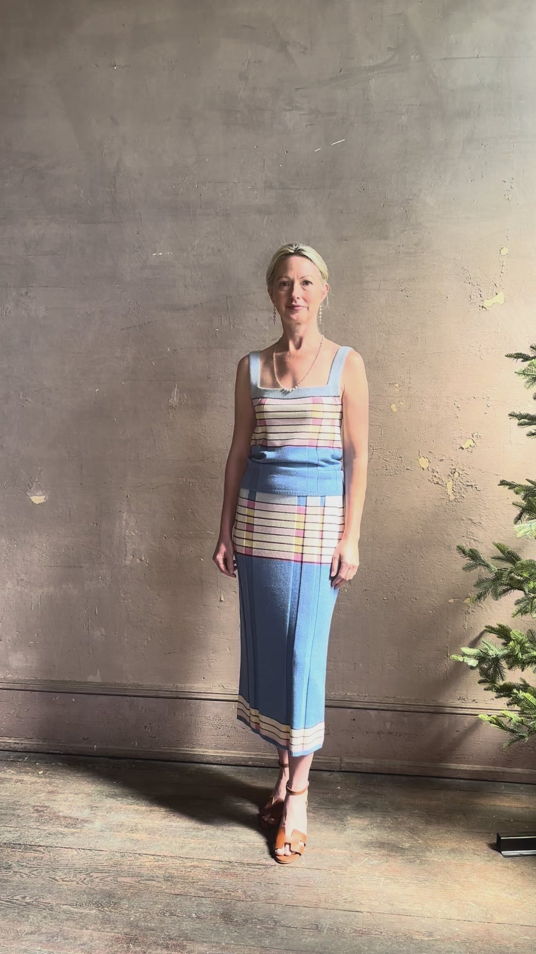 Mature woman reviewing Plaited Rib knit pencil Skirt from Guest in Residence rendered in delft blue and crafted from a luxurious blend of silk, linen, nylon, and elastane with wide rib texture down front and back with pink and yellow horizontal stripes at hips and bottom edge