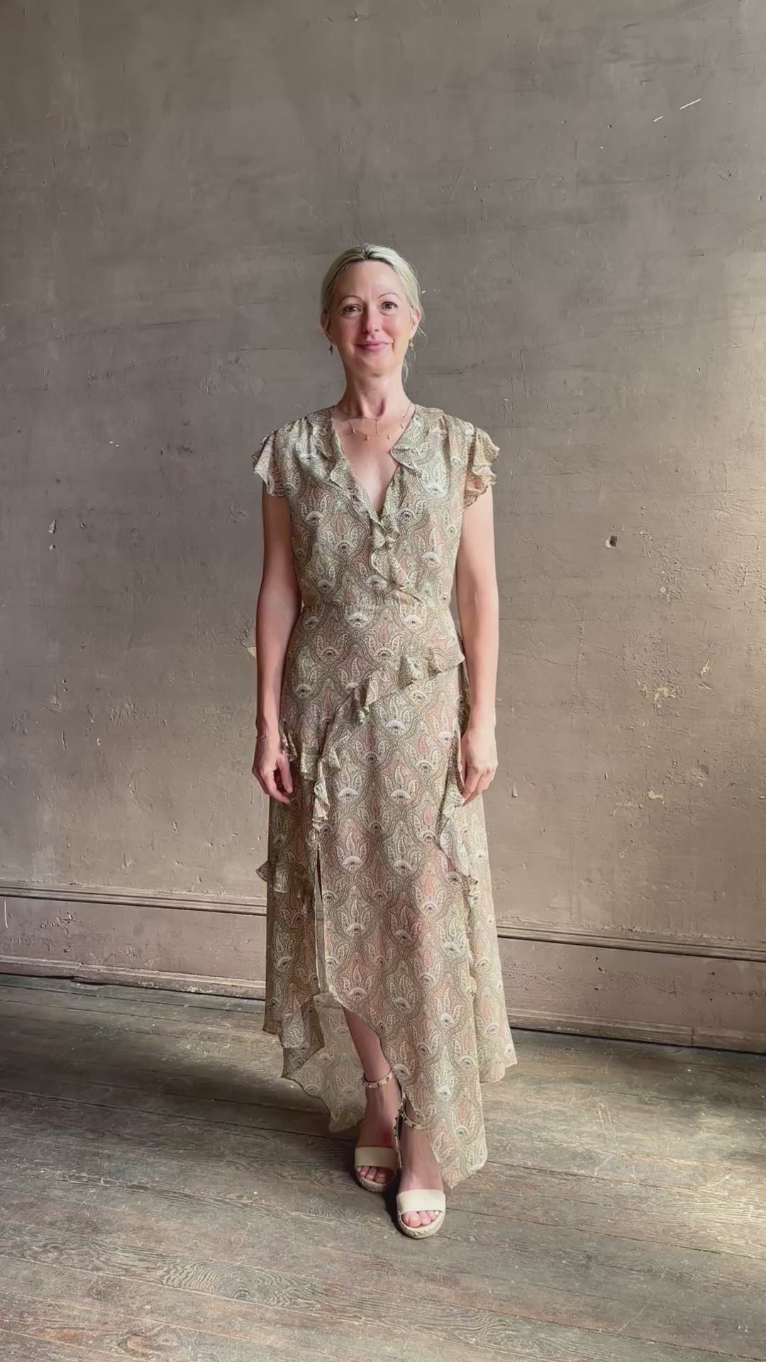 Mature woman reviewing the Cap Sleeve Anenel maxi Dress from luxury designer Veronica Beard rendered in a soft khaki, green, and pink paisley print and crafted in silk with cap sleeves, v- neckline, and asymmetrical hem all finished with soft feminine ruffles in a timeless A-line silhouette