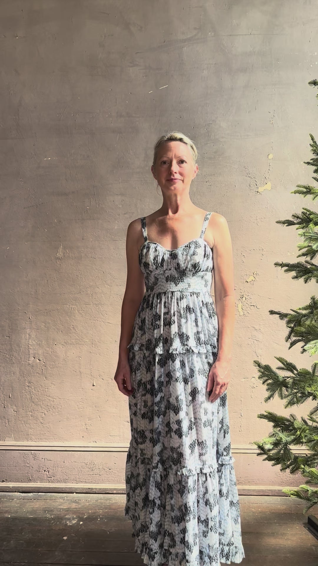Mature woman reviewing Ophelia Cami Cotton maxi Dress from Ulla Johnson rendered in a crisp white ground adorned with a soft black and light blue print and crafted from a cotton and viscose blend with an empire waist, sweatheart neckline and spaghetti straps