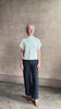 Mature woman reviewing refined Mock Neck Tee Blouse from TWP rendered in a subtle sea glass blue hue and crafted from a viscose linen blend made in the USA, with short sleeves, asymmetrical design and quality fabric draping