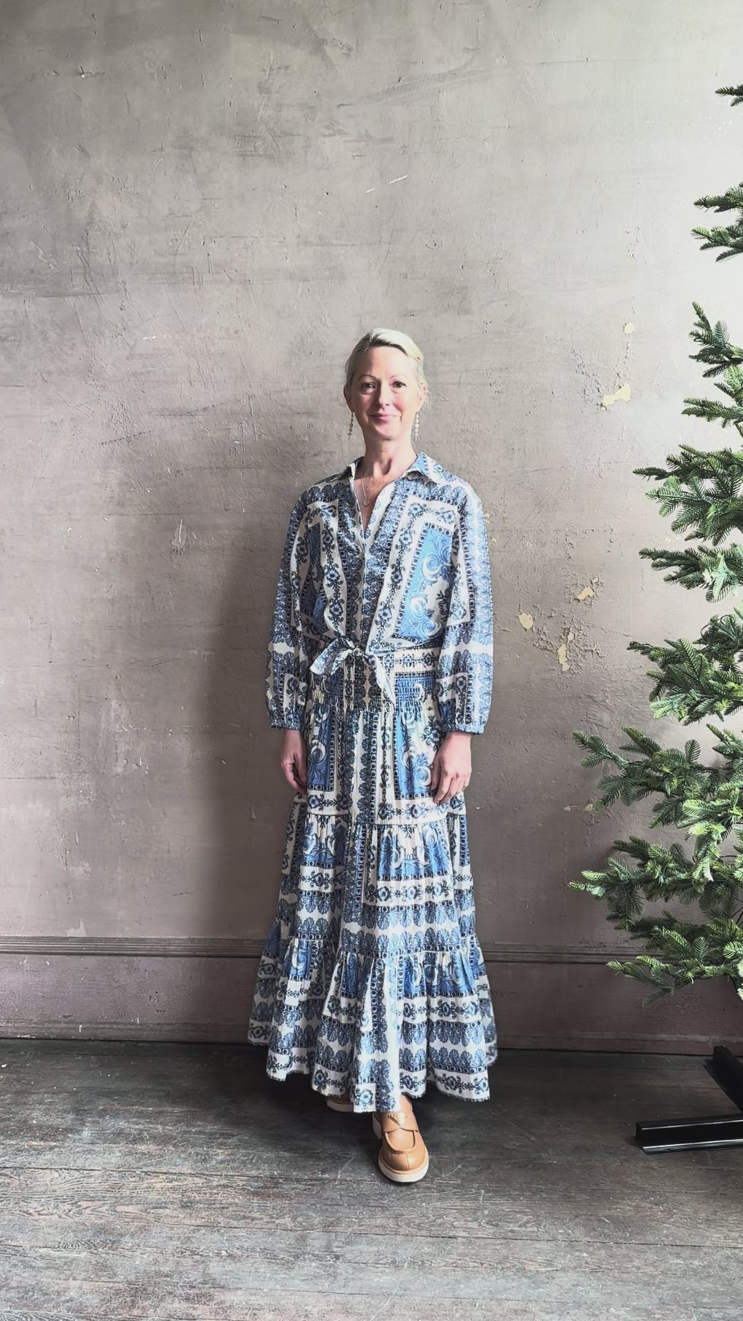 Mature woman reviewing the Rumson Top from Cara Cara rendered in a blue and white Hudson Scarf Sky print and crafted from 100% cotton with long sleeves, button down v- neck and tie front cropped top