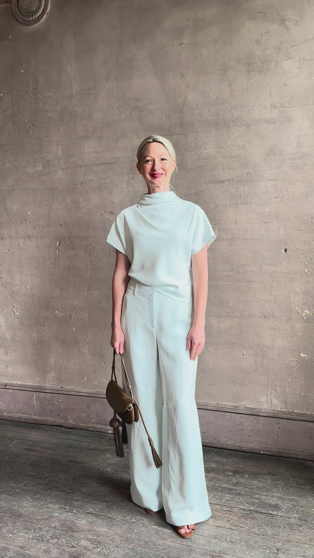 Mature woman reviewing the Dylan Pant from TWP rendered in a sea glass blue hue and crafted from a viscose and linen blend, made in the USA, this luxury mid-rise trouser offers a wide leg silhouette with hidden seam side and back pockets 