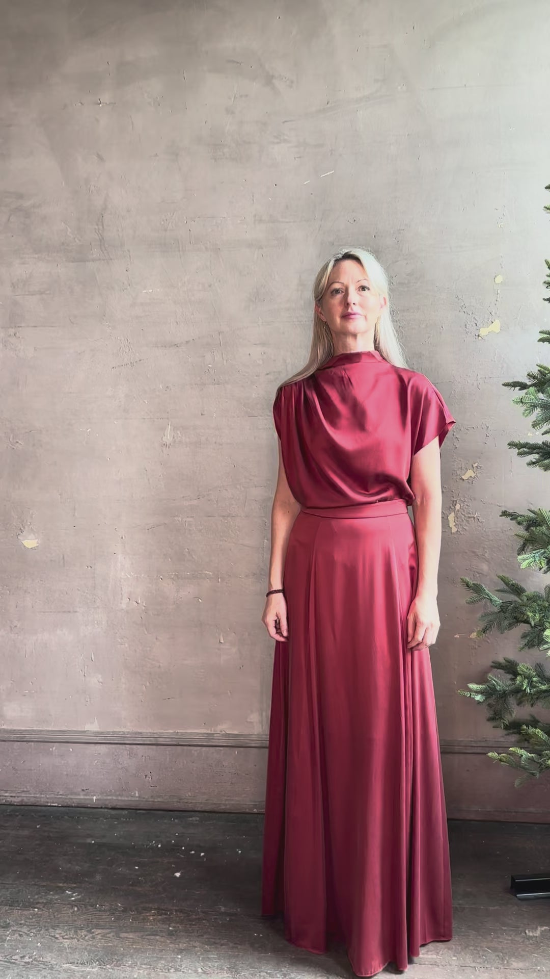 Mature woman reviewing Wish You Would blouse from TWP rendered in a rich currant red and crafted from a luxurious silk blend with a mock neck,  asymetrical design and draping short sleeves shoulder button closure