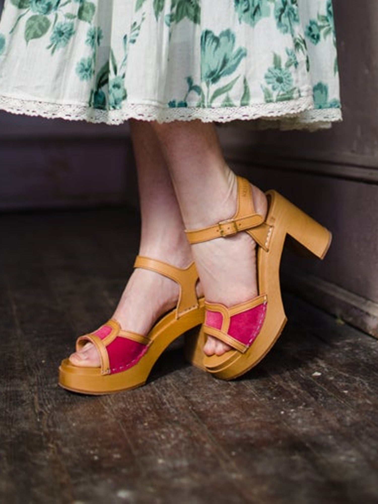 Image featuring a woman wearing  the clogs by Swedish Hasbeens in brown leather with a wood platform sole, pink suede, buckle closure and a block heel.