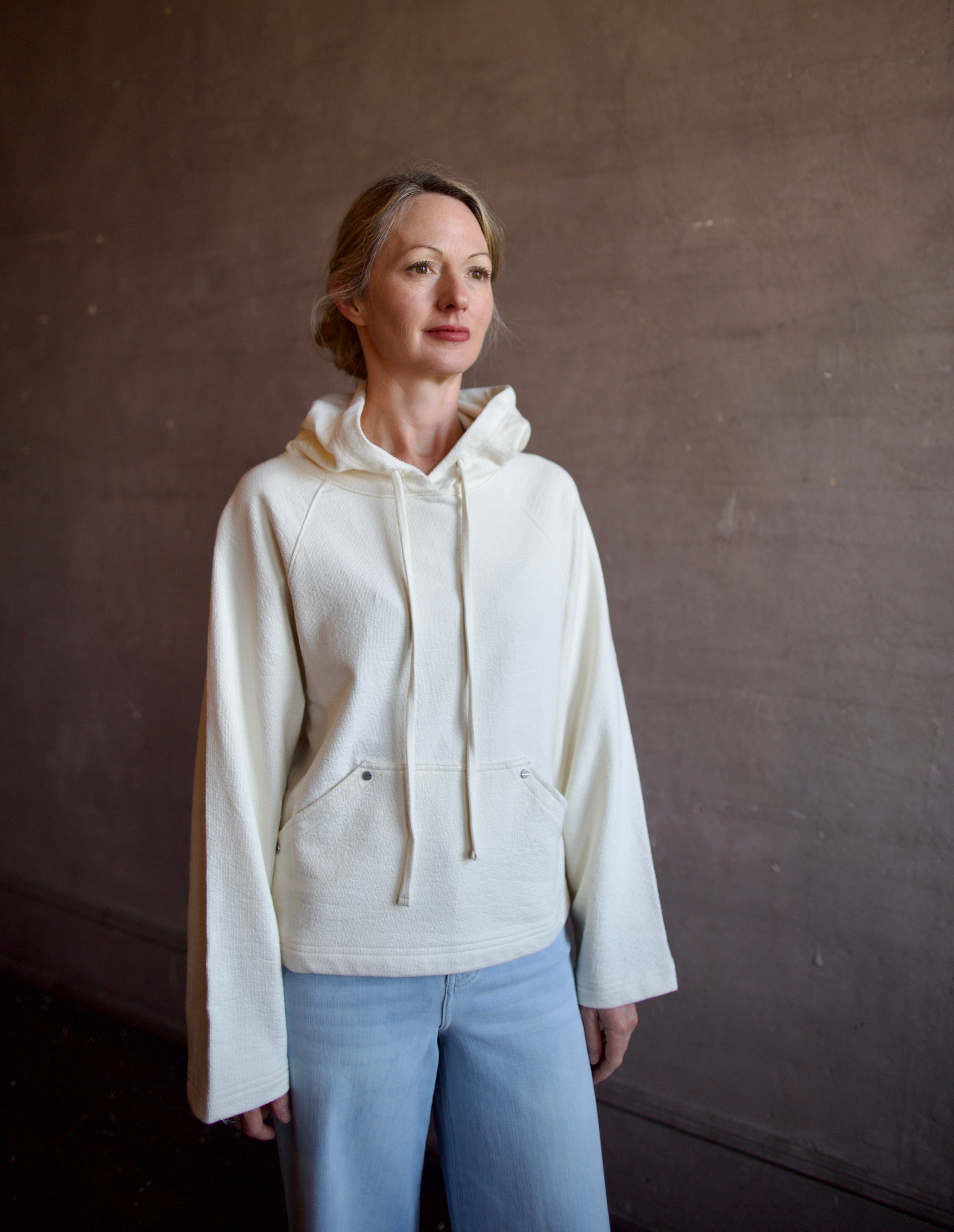 Mature woman wearing luxury TWP Ali's ivory Hoodie featuring raglan sleeves and kangaroo pocket with boxy fit, delivering elevated comfort