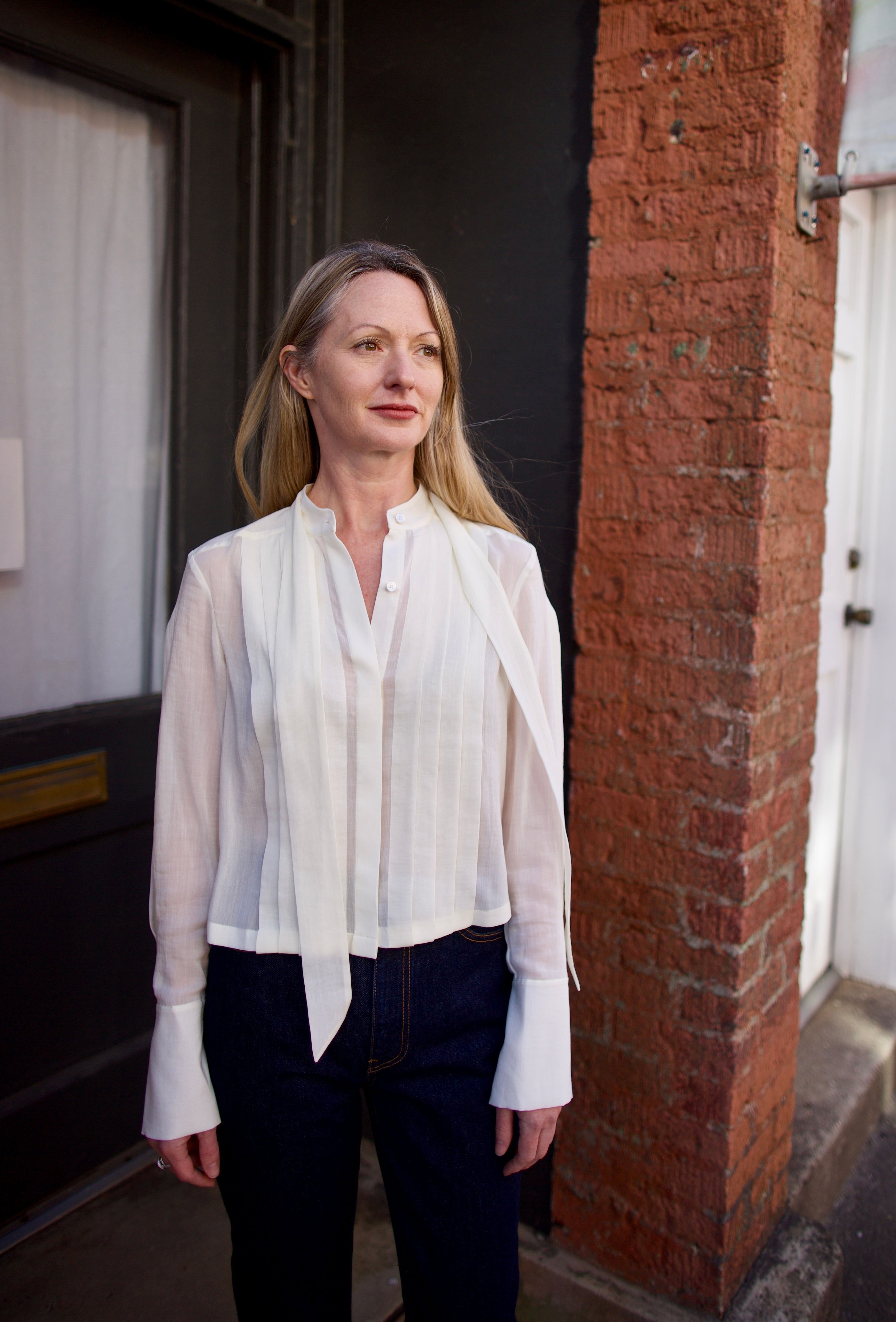 Mature woman wearing elegant luxury women's ivory cotton-silk Patti blouse by TWP with front pleats and buttons  in a slightly cropped fit