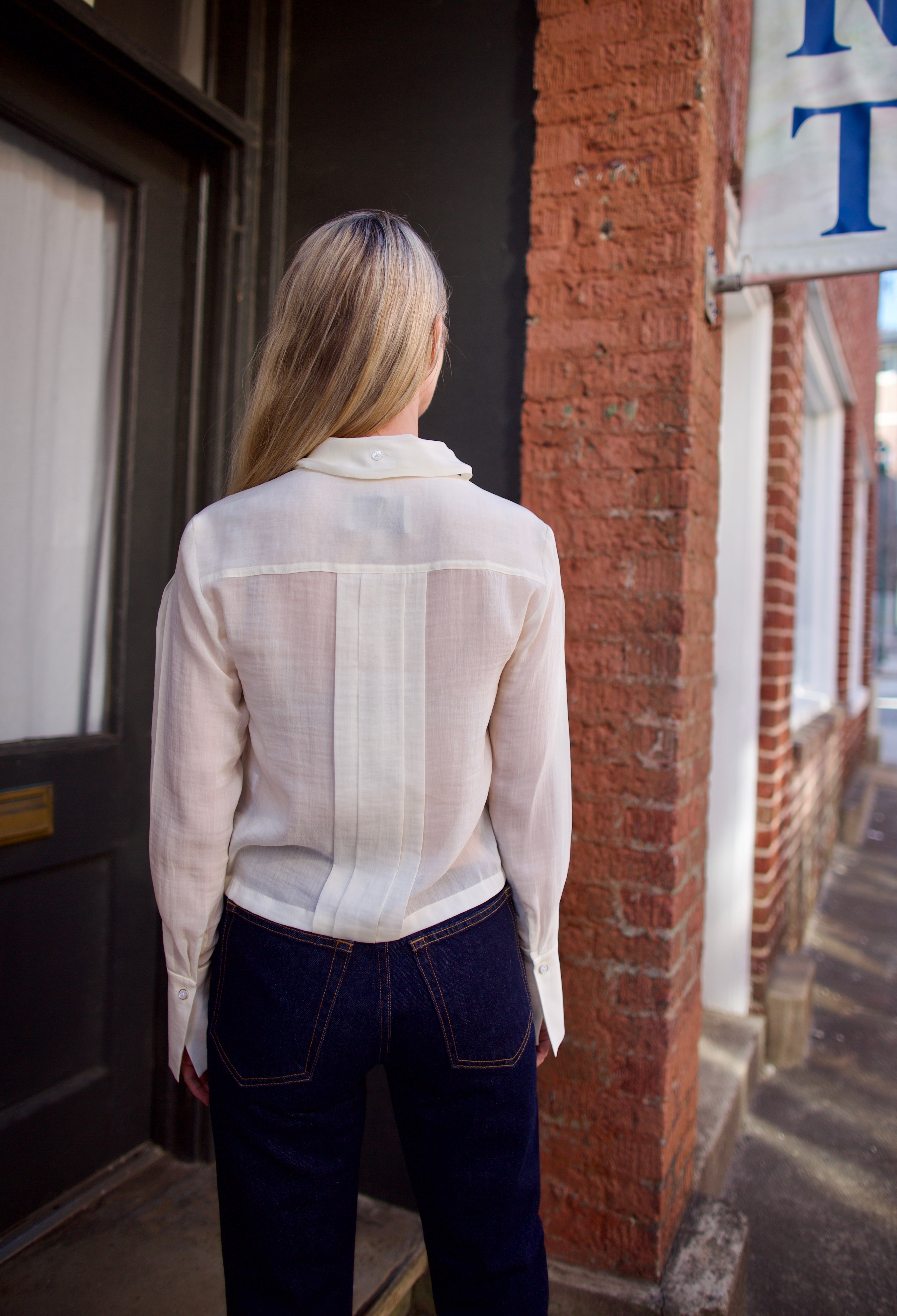 Mature woman wearing elegant luxury women's ivory cotton-silk Patti blouse by TWP with front pleats and buttons  in a slightly cropped fit