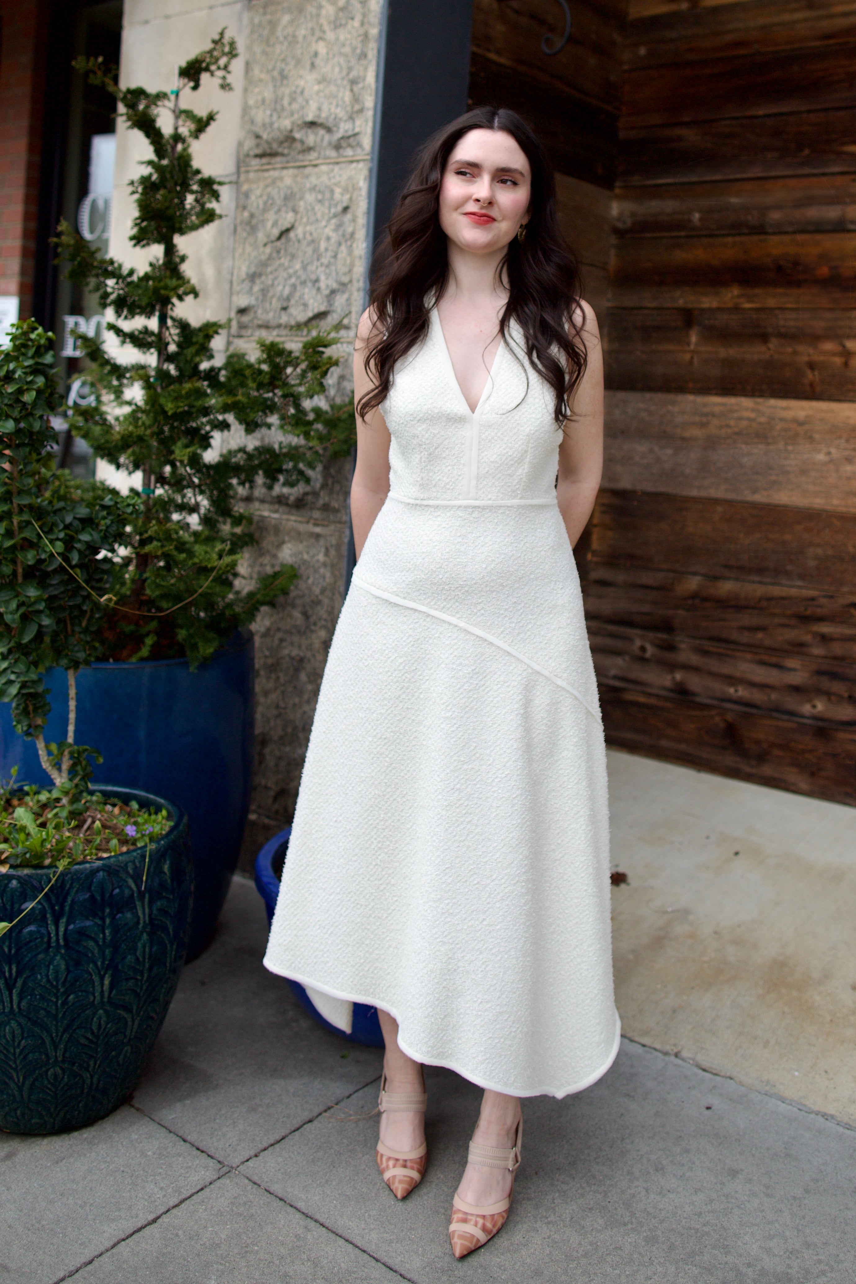 Woman wearing Ulla Johnson Florence Dress in textured off-white cotton blend with a v-neckline asymmetrical hem and v-neckline
