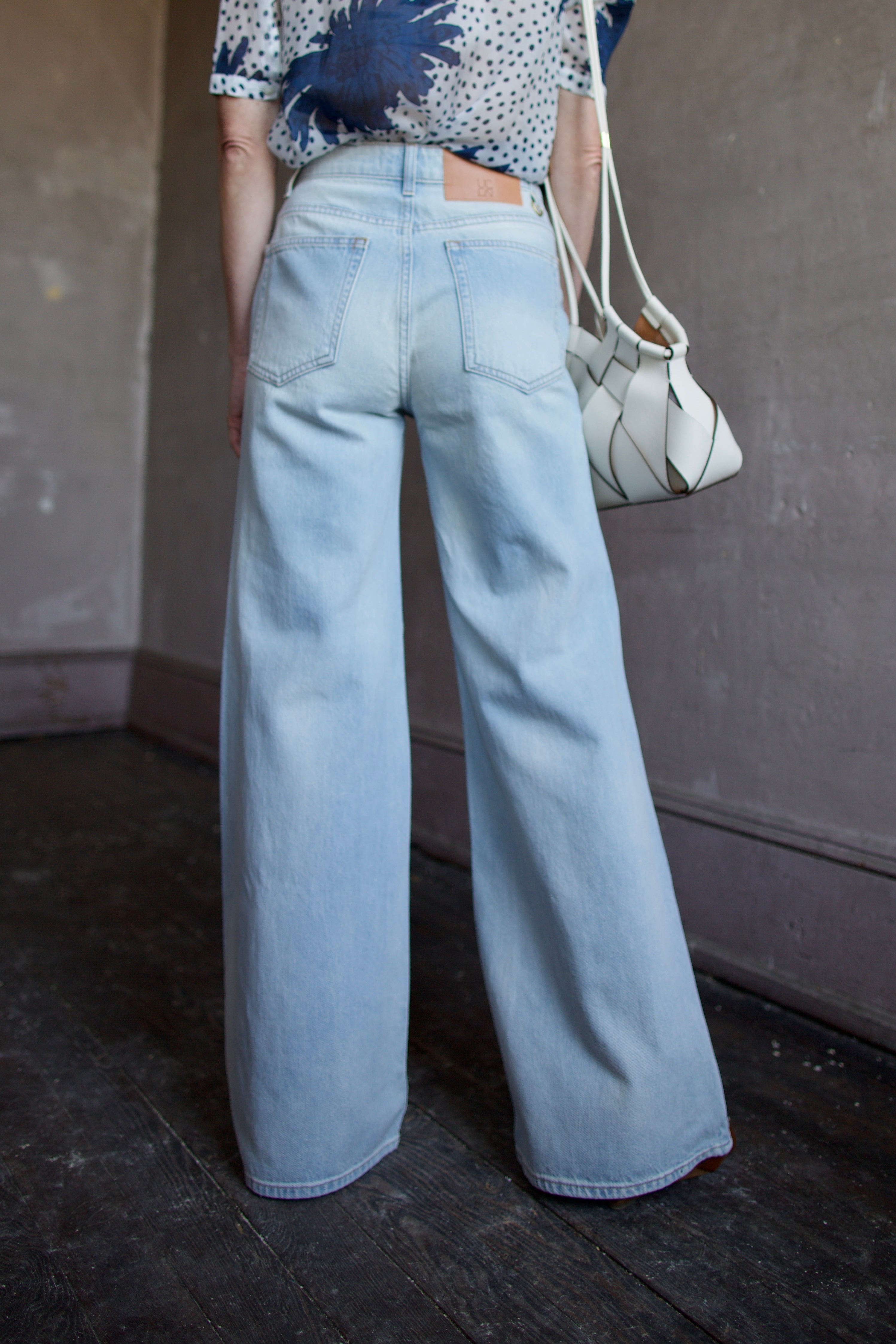 Mature woman wearing Ulla Johnson Gwynne Cielo Jeans in recycled cotton gold button fly light wash front pockets